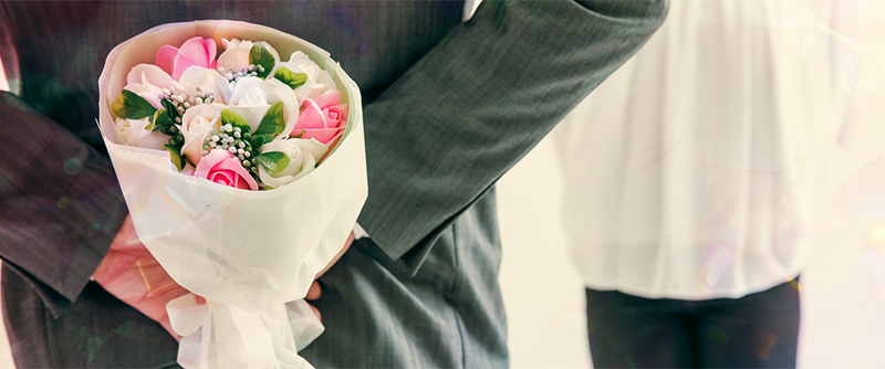 プレゼント用の花束を後ろ手に持つ男性